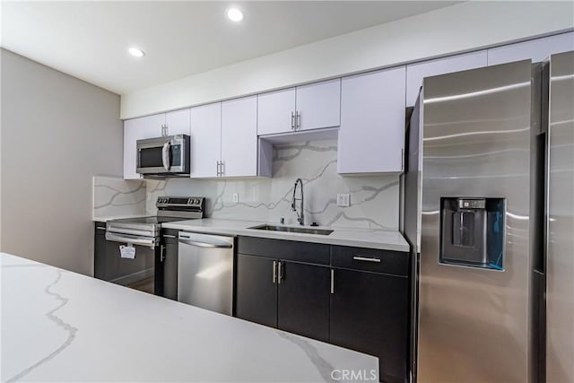 kitchen with appliances with stainless steel finishes, a sink, backsplash, white cabinets, and recessed lighting