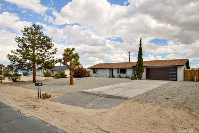 ranch-style house featuring a garage, concrete driveway, and fence