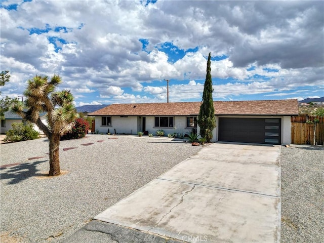 ranch-style home with stucco siding, an attached garage, driveway, and fence