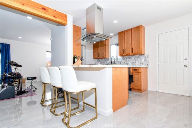kitchen featuring island exhaust hood, brown cabinetry, a breakfast bar area, tasteful backsplash, and light countertops