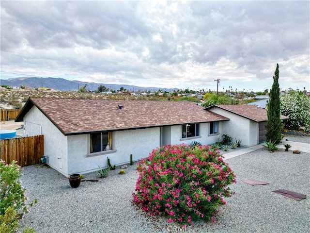 single story home featuring fence, stucco siding, a shingled roof, and a mountain view