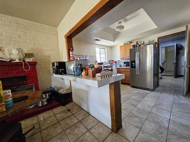 kitchen featuring stainless steel fridge, a peninsula, a tray ceiling, light countertops, and light tile patterned floors