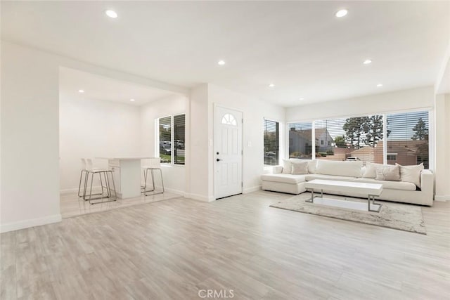 living area featuring baseboards, recessed lighting, light wood finished floors, and a bar