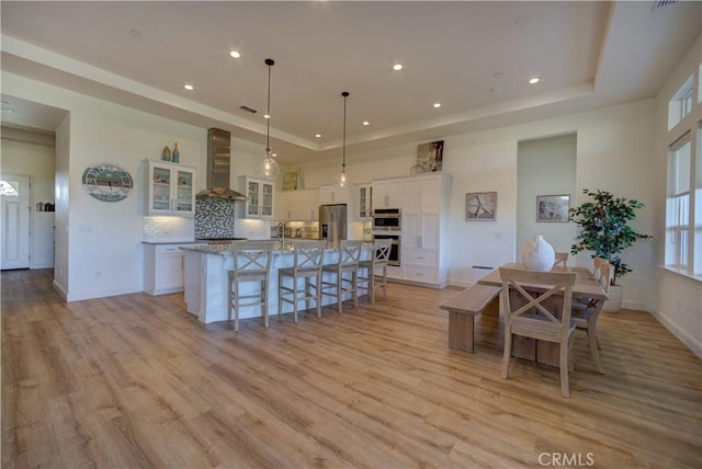 851 Trail View Pl, Nipomo, CA 93444 - kitchen with wall chimney range hood, a raised ceiling, white cabinetry, a kitchen breakfast bar, and recessed lighting