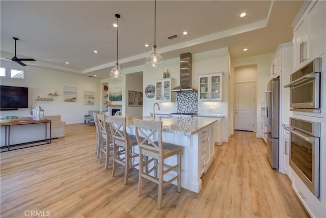 851 Trail View Pl, Nipomo, CA 93444 - kitchen featuring wall chimney exhaust hood, a tray ceiling, open floor plan, white cabinetry, and light wood finished floors