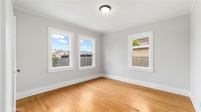 empty room with ornamental molding, baseboards, and light wood-style floors