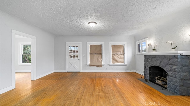 unfurnished living room featuring hardwood / wood-style flooring, a textured ceiling, baseboards, and a fireplace