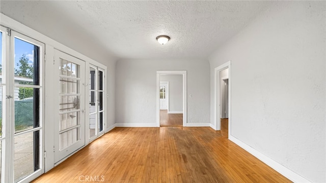 unfurnished room with a textured ceiling, light wood-type flooring, and baseboards