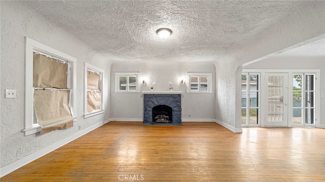 unfurnished living room with a textured wall, a textured ceiling, hardwood / wood-style flooring, baseboards, and a fireplace