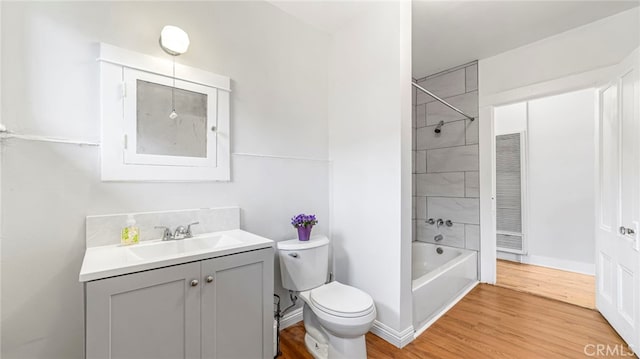 bathroom with toilet, vanity, wood finished floors,  shower combination, and baseboards
