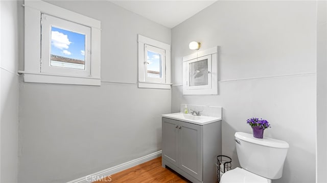 half bath with vanity, toilet, wood finished floors, and baseboards