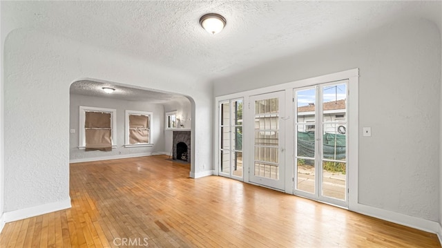 unfurnished living room with a textured ceiling, a fireplace with flush hearth, a textured wall, hardwood / wood-style flooring, and baseboards