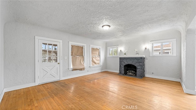 unfurnished living room featuring a textured wall, a textured ceiling, hardwood / wood-style flooring, a stone fireplace, and baseboards