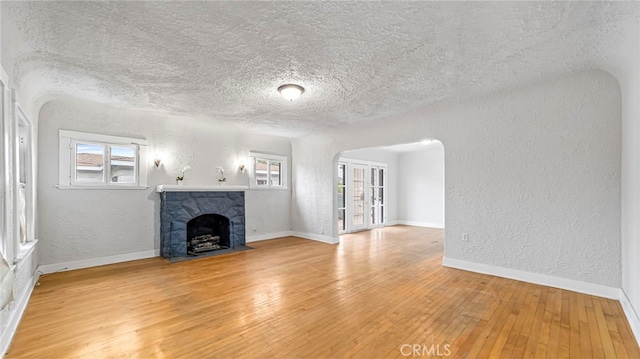unfurnished living room with a textured wall, light wood-type flooring, a textured ceiling, arched walkways, and a fireplace