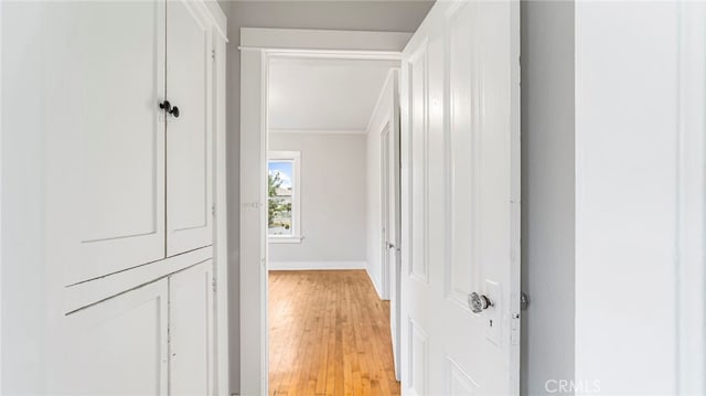 hallway featuring ornamental molding, light wood-style floors, and baseboards