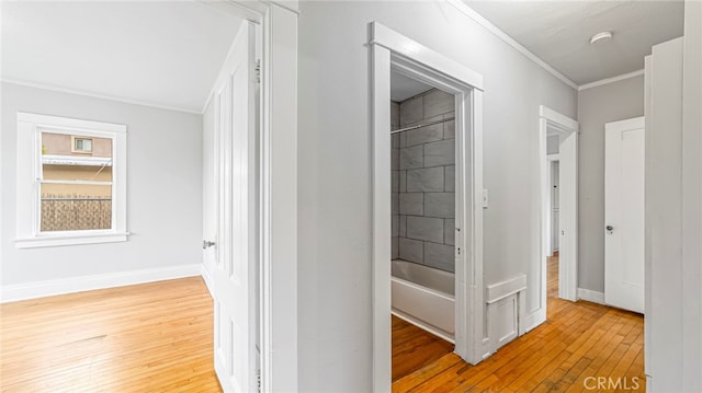 hallway with light wood-style floors, baseboards, and crown molding