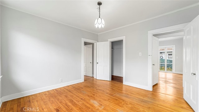 unfurnished bedroom featuring light wood-style flooring, baseboards, crown molding, and a closet