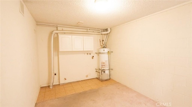 spare room featuring water heater, a textured ceiling, light tile patterned flooring, concrete block wall, and light colored carpet