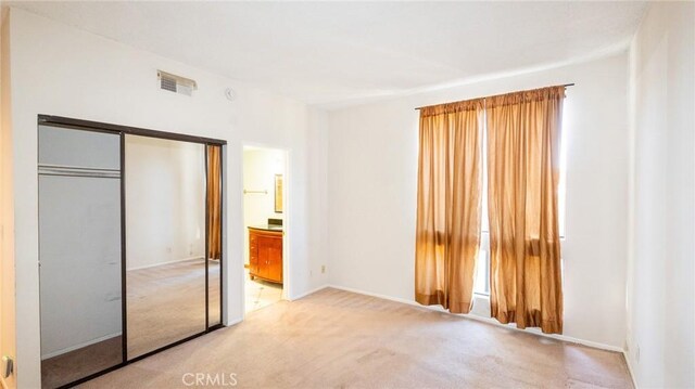 unfurnished bedroom with carpet, a closet, baseboards, and ensuite bathroom