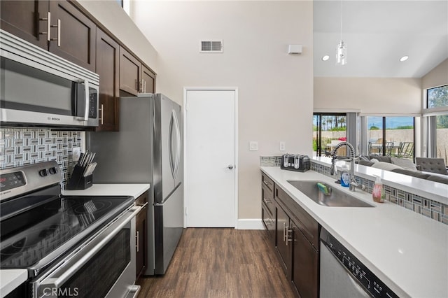 kitchen with stainless steel appliances, a sink, a towering ceiling, dark wood finished floors, and dark brown cabinets