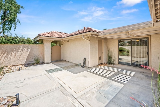 doorway to property featuring stucco siding, a patio area, a tiled roof, and fence
