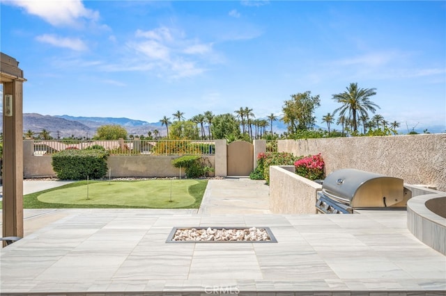 view of patio featuring a putting green, a fenced backyard, grilling area, a fire pit, and a mountain view