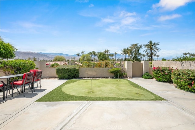 fenced backyard featuring a putting green, a patio area, and a mountain view
