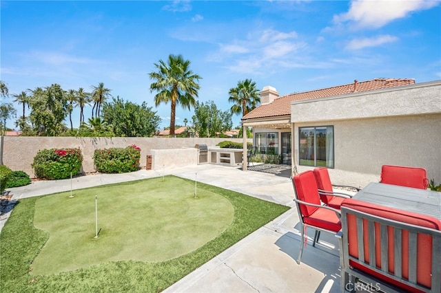 fenced backyard with a putting area, a patio, and area for grilling