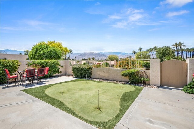 fenced backyard with an area to practice putting, a patio area, a mountain view, and a gate