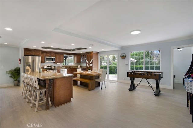 kitchen featuring appliances with stainless steel finishes, light wood-type flooring, baseboards, a kitchen breakfast bar, and ornamental molding