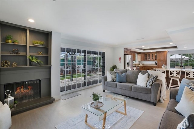 living room featuring plenty of natural light, light wood-style floors, a raised ceiling, a large fireplace, and recessed lighting