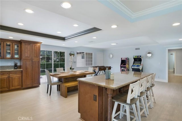 kitchen with crown molding, a tray ceiling, a breakfast bar area, light wood-style floors, and brown cabinets