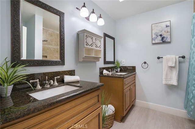 bathroom with two vanities, a shower, baseboards, and wood finished floors
