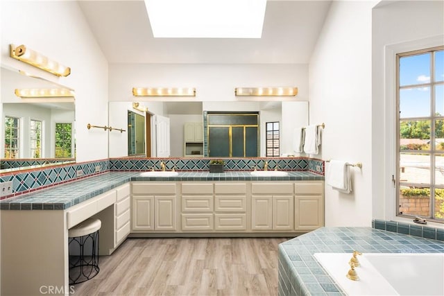 23721 Sarda Rd, Valencia, CA 91355 - bathroom featuring double vanity, backsplash, a bath, wood finished floors, and a skylight