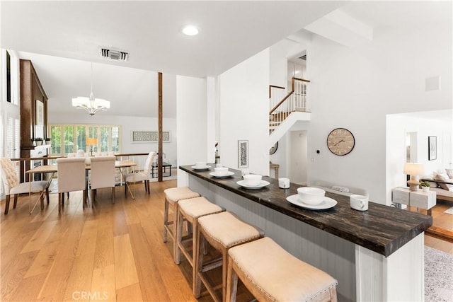 23721 Sarda Rd, Valencia, CA 91355 - kitchen featuring light wood-style floors, dark countertops, a towering ceiling, a chandelier, and a breakfast bar