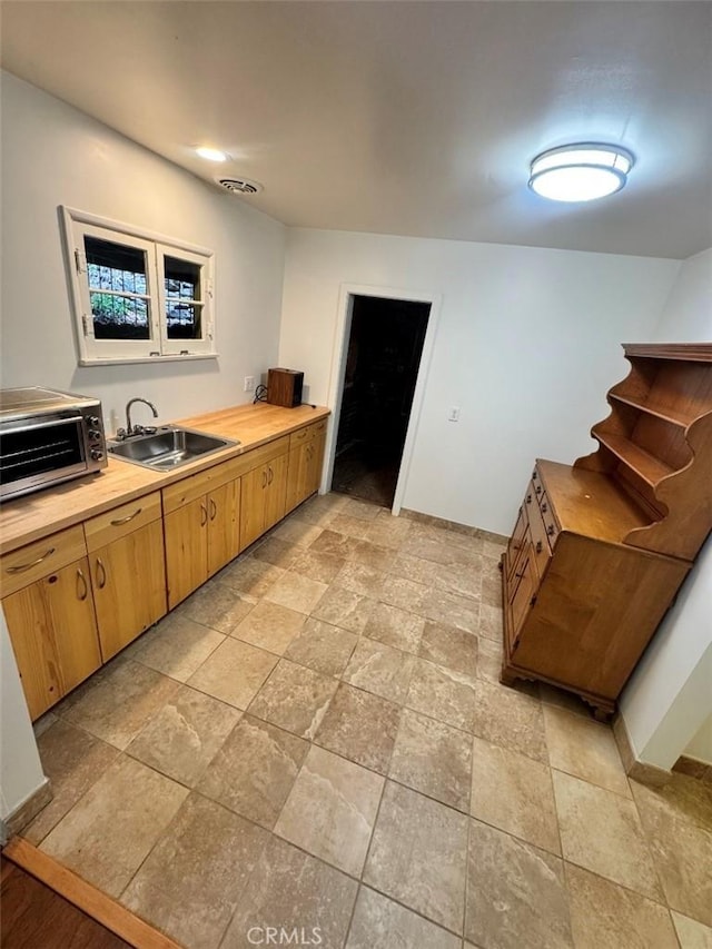 kitchen featuring a sink, light stone finish flooring, butcher block counters, and baseboards