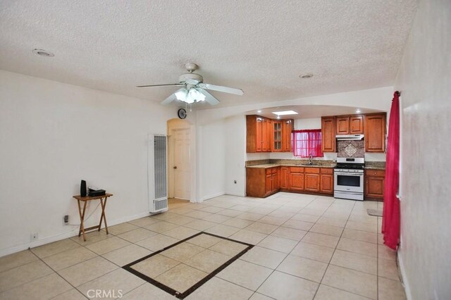 2851 Webster Ave, Long Beach, CA 90810 - kitchen featuring stainless steel range with gas stovetop, a heating unit, brown cabinetry, under cabinet range hood, and a textured ceiling