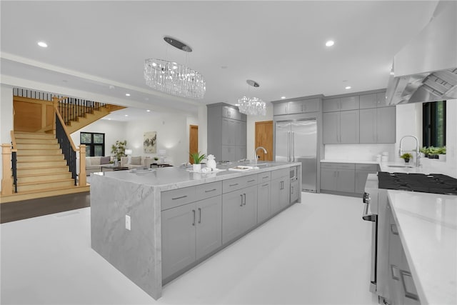 kitchen with gray cabinets, high quality appliances, wall chimney exhaust hood, a chandelier, and a sink
