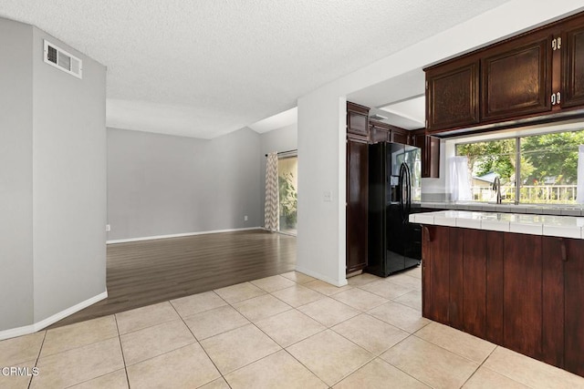 817 Copper Privado, Ontario, CA 91762 - kitchen with black fridge, tile counters, light tile patterned flooring, dark brown cabinetry, and a textured ceiling