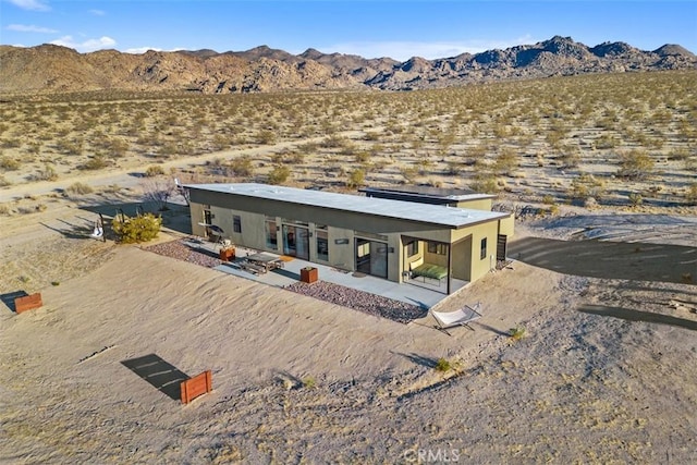 back of house featuring a mountain view, view of desert landscape, a patio, and a rural view