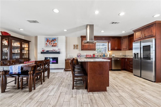 5471 Santa Gertrudes Ave, Garden Grove, CA 92845 - kitchen featuring stainless steel appliances, island range hood, light wood-style floors, a glass covered fireplace, and a breakfast bar