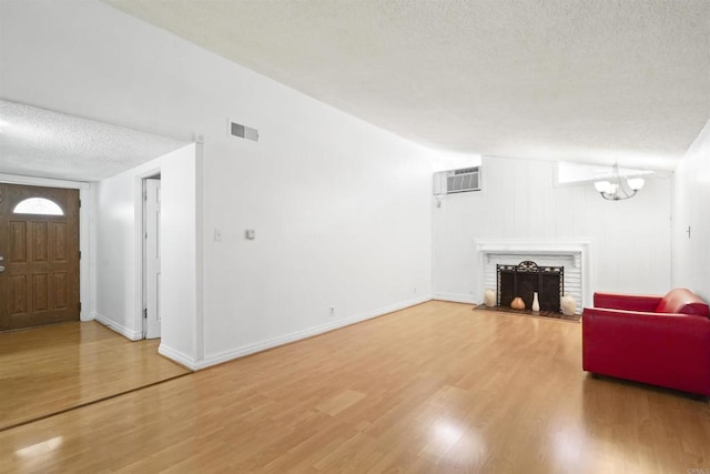 17010 Pocono St, La Puente, CA 91744 - living room with a textured ceiling, an AC wall unit, light wood finished floors, a brick fireplace, and a chandelier