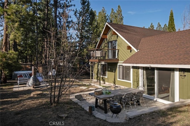 back of property with a balcony, a patio area, and roof with shingles