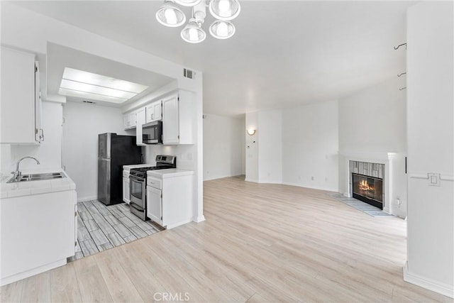21848 S Vermont Ave Unit 6, Torrance, CA 90502 - kitchen featuring appliances with stainless steel finishes, light wood-style floors, open floor plan, a tiled fireplace, and white cabinetry