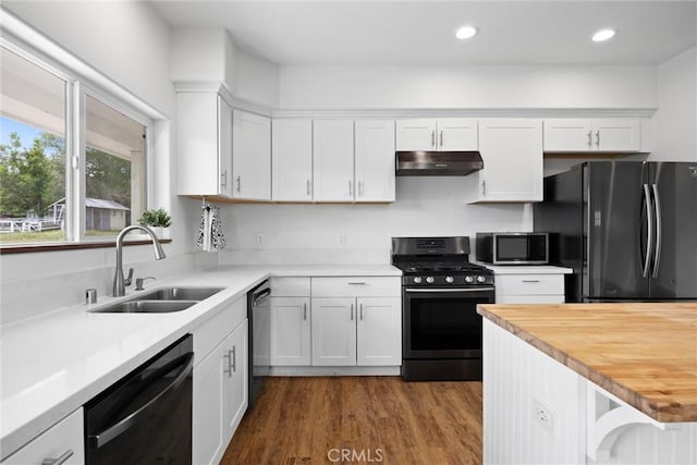 kitchen with black appliances, a sink, under cabinet range hood, white cabinetry, and dark wood-style flooring