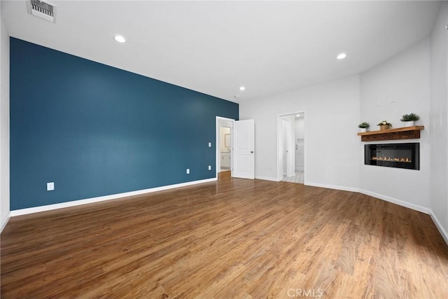 unfurnished living room featuring a glass covered fireplace, wood finished floors, baseboards, and recessed lighting