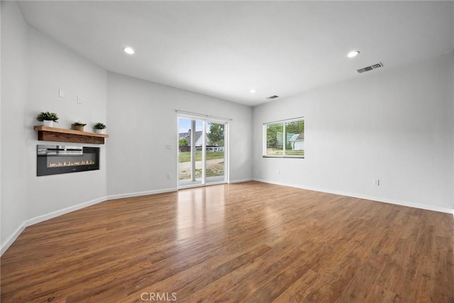 spare room featuring a glass covered fireplace, wood finished floors, recessed lighting, and baseboards