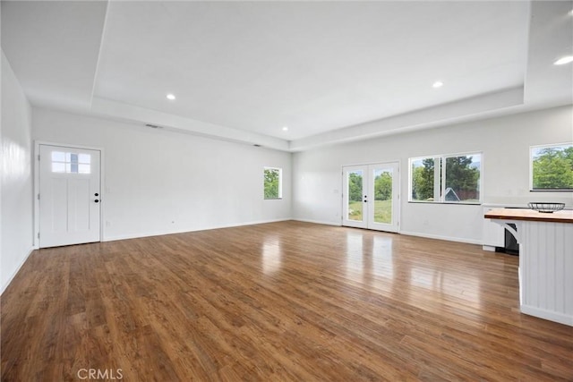 unfurnished living room featuring a tray ceiling, wood finished floors, recessed lighting, and baseboards