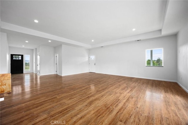 unfurnished living room with wood finished floors, recessed lighting, baseboards, and a tray ceiling