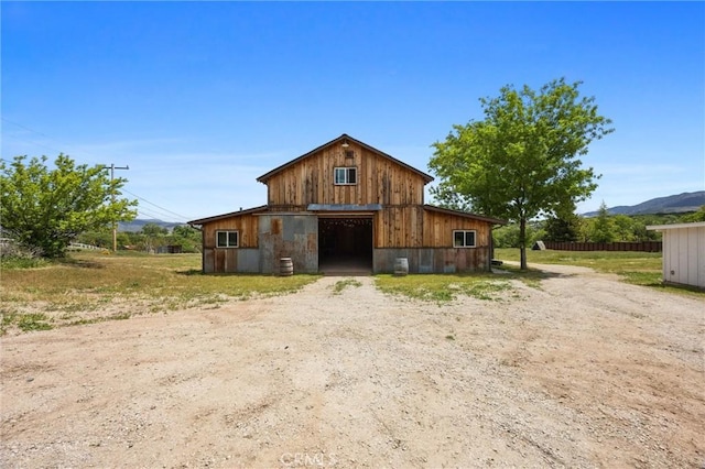 rear view of property with a barn, a detached garage, dirt driveway, an outbuilding, and a mountain view